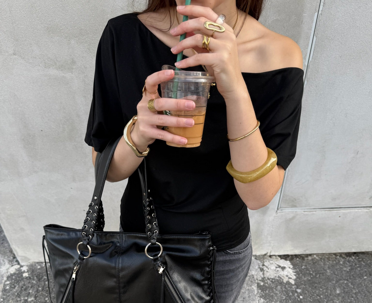 Mujer con joyas de acero dorado, bolso negro y top negro, sosteniendo bebida fría