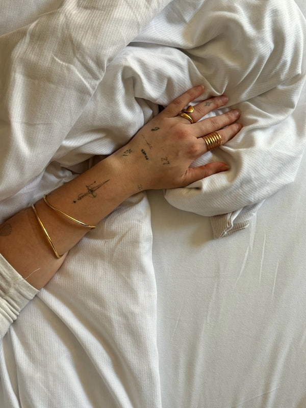 Pulsera Tiana en dorado de acero inoxidable sobre el brazo de una mujer apoyado en sabanas blancas