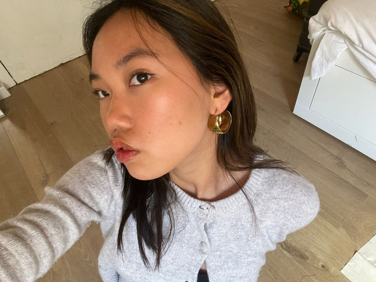 Mujer con aretes de aro grandes dorados de acero hipoalergénico en interior moderno