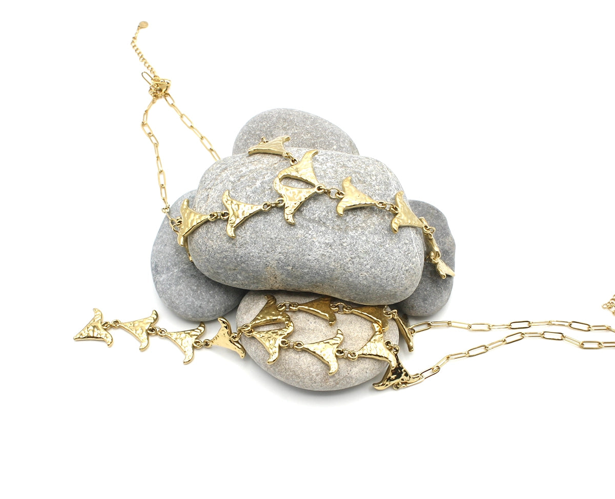 Collar Grace acero inoxidable dorado, sobre rocas de mar, formas onduladas y textura martillada que reflejan la luz de forma única, material resistente e hipoalergénico. DELACABRA.COM