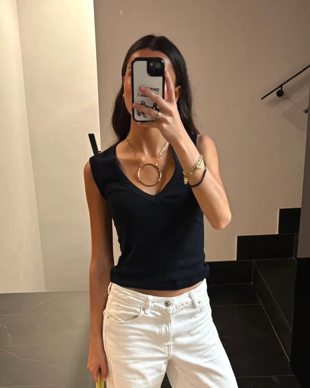 Collar Charlotte acero inoxidable dorado, mujer luciendo la joya con una camiseta con cuello en V azul, combinado con pulseras, anillos y otros accesorios. DELACABRA.COM