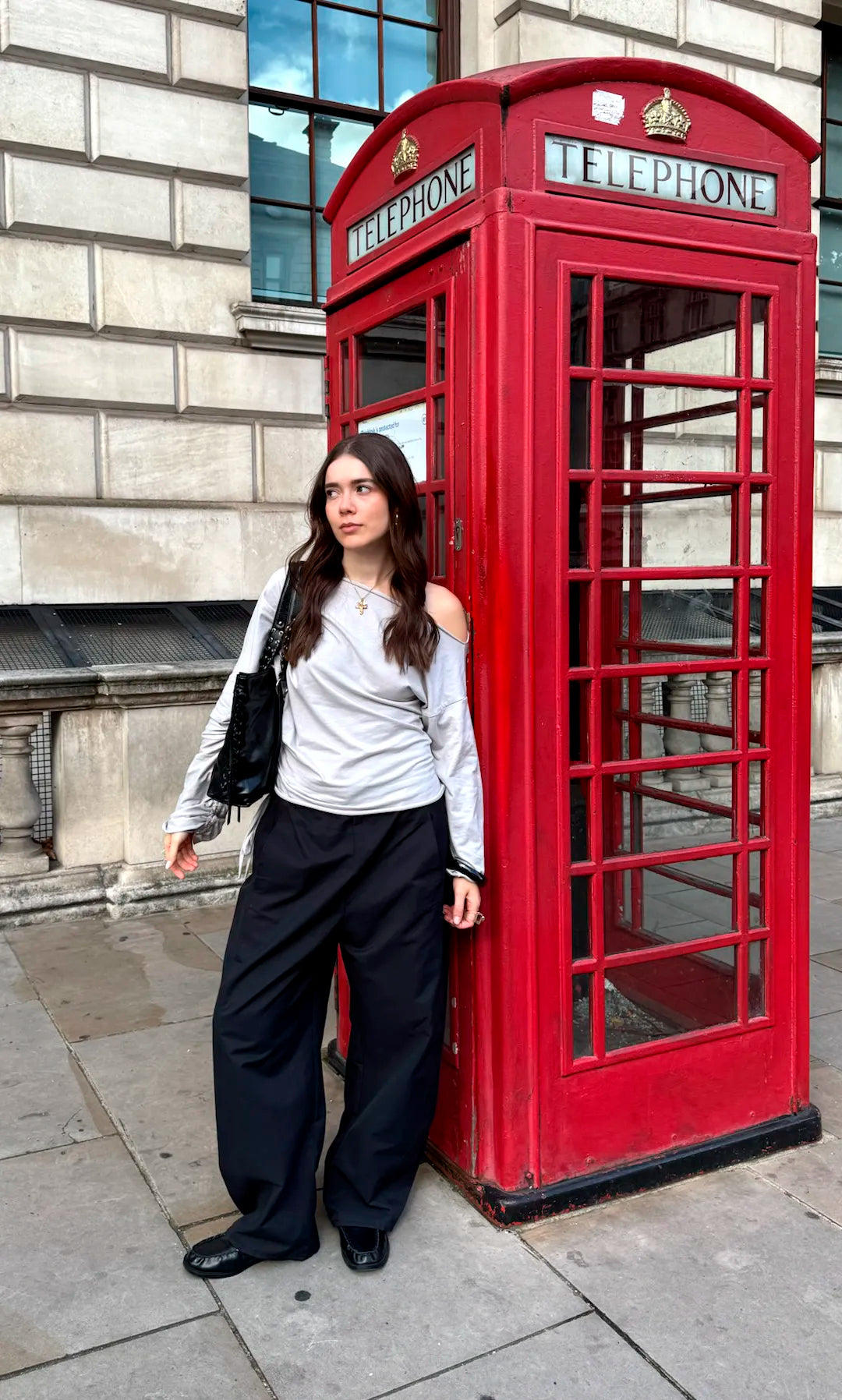 Collar Multicruz acero inoxidable dorado en una modelo en la calle al lado de una cabina de teléfono, jersery gris. DELACABRA