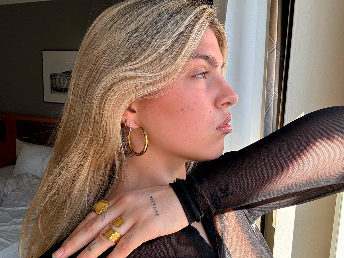 Pendientes Aro Basics acero inoxidable dorado, modelo luciendo conjunto de otros aritos y anillos de delacabra.com, brillo y elegancia sin igual. - DELACABRA