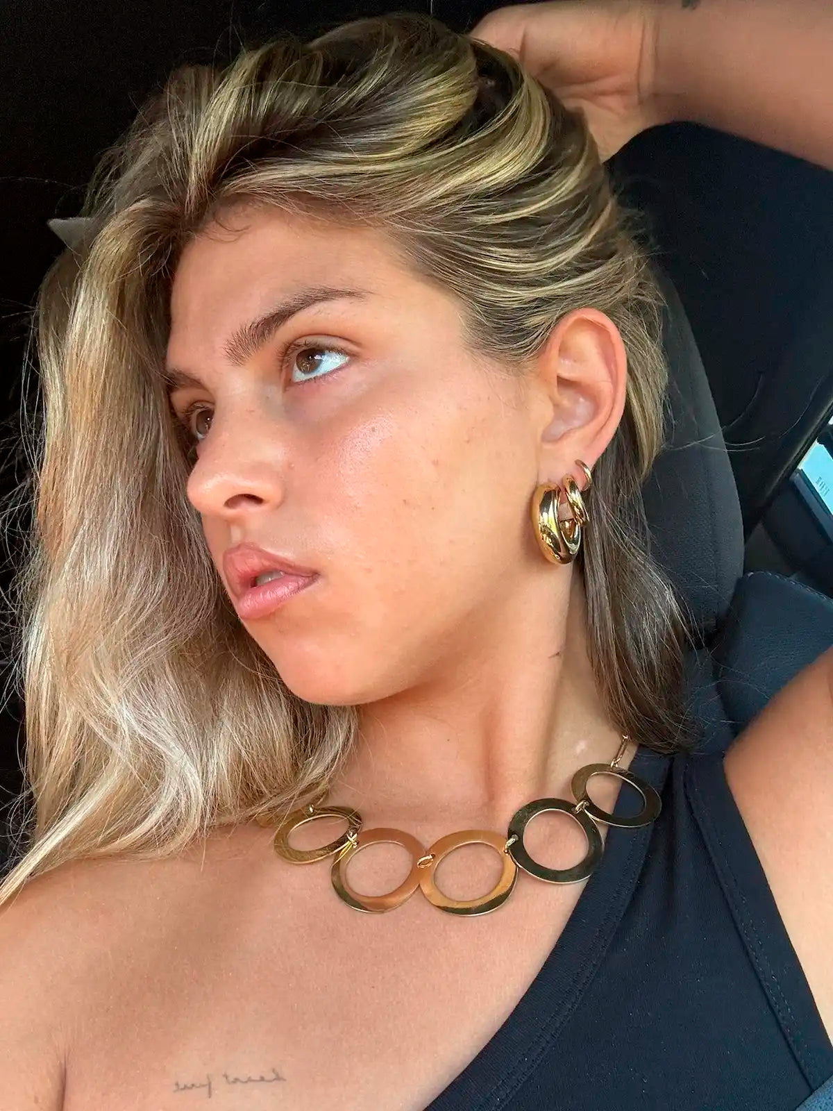 Mujer luciendo pendiente de aro grande de acero inoxidable dorado y collar a juego, estilo moderno.