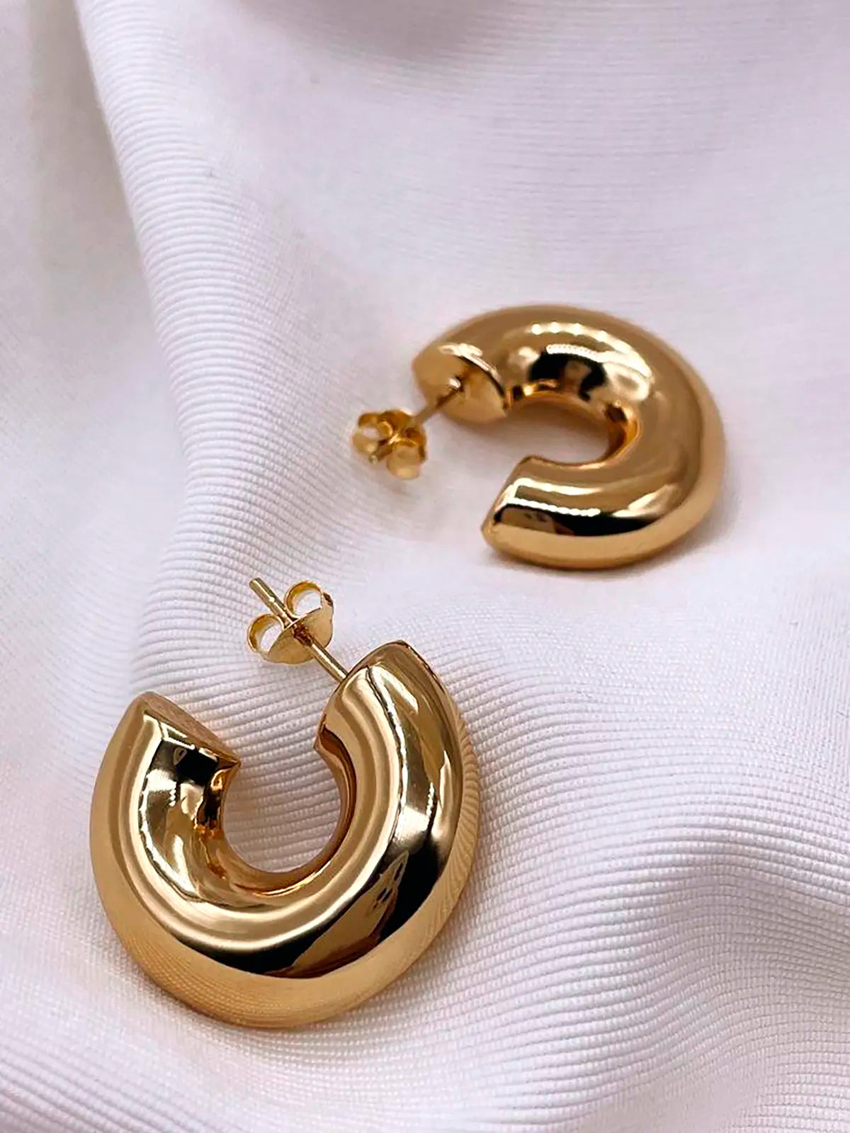 Pendientes aro grandes de acero inoxidable dorado sobre tela blanca, joyas modernas y hipoalergénicas.