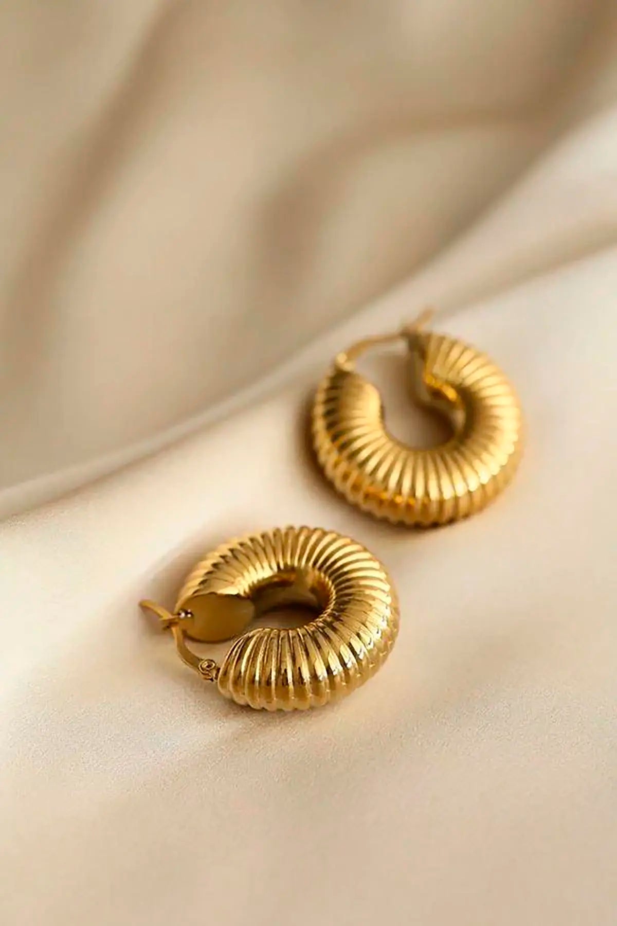 Pendientes aro dorados de acero inoxidable, diseño grueso y acanalado, sobre tela beige.