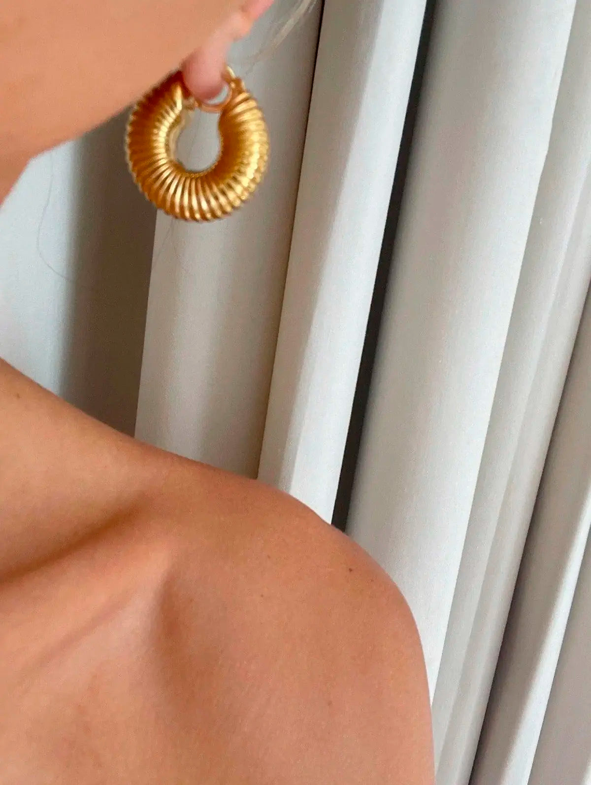 Pendiente aro dorado de acero inoxidable con textura acanalada, llevado en la oreja de una mujer.