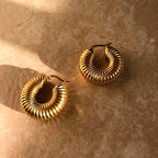 Pendientes de aro dorados de acero inoxidable con textura acanalada sobre fondo beige