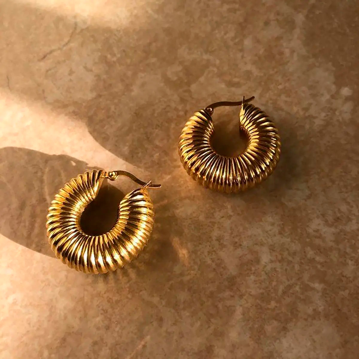 Pendientes de aro dorados de acero inoxidable con textura acanalada sobre fondo beige