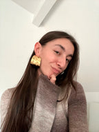 Pendientes Leaf acero inoxidable dorado, mujer luciendo los pendientes con atuendo casual, jersey gris en varios tonos y cabello largo. - DELACABRA