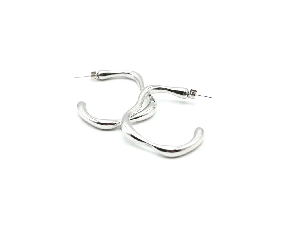 Pareja de aros Caudal plata resaltando su diseño de arco minimalista. Joya de acero amable con la piel DELACABRA.