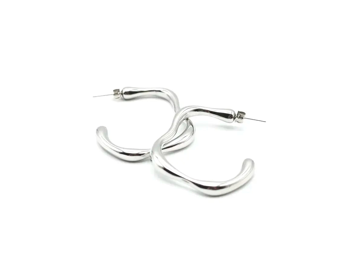 Pareja de aros Caudal plata resaltando su diseño de arco minimalista. Joya de acero amable con la piel DELACABRA.