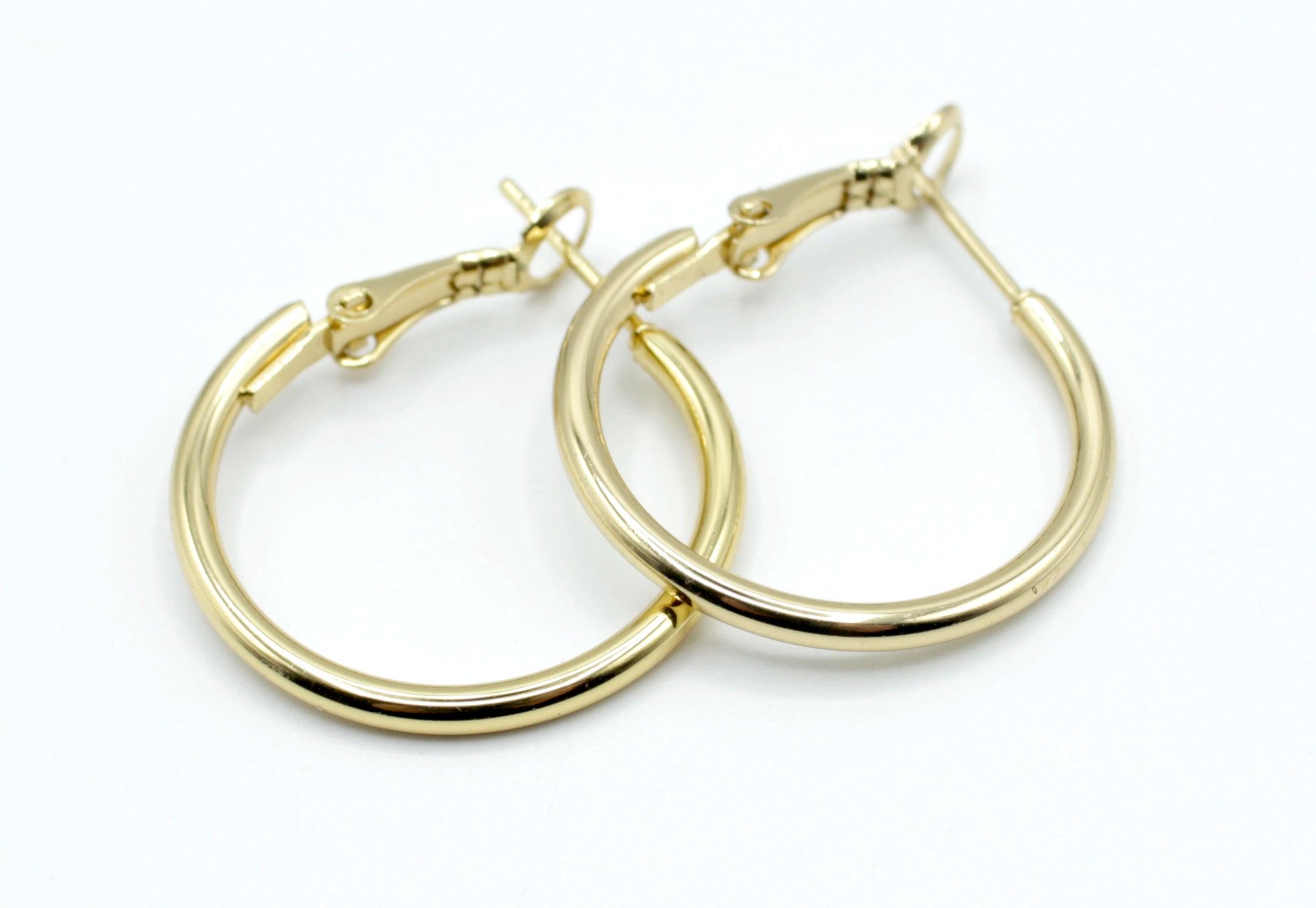 Pendientes de aro mini dorados de acero inoxidable sobre fondo blanco, joyería moderna.