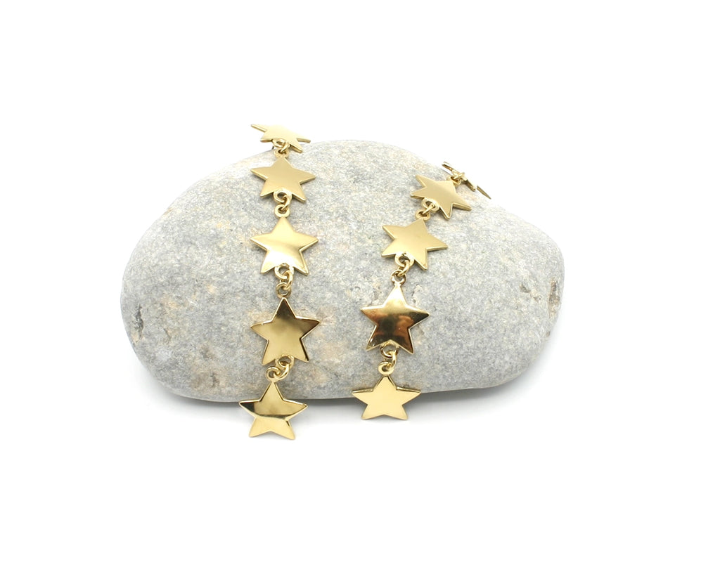 Pendientes largos Georgina acero inoxidable dorado sobre una roca de rio, estrellas doradas brillantes unidas en cascada. DELACABRA 