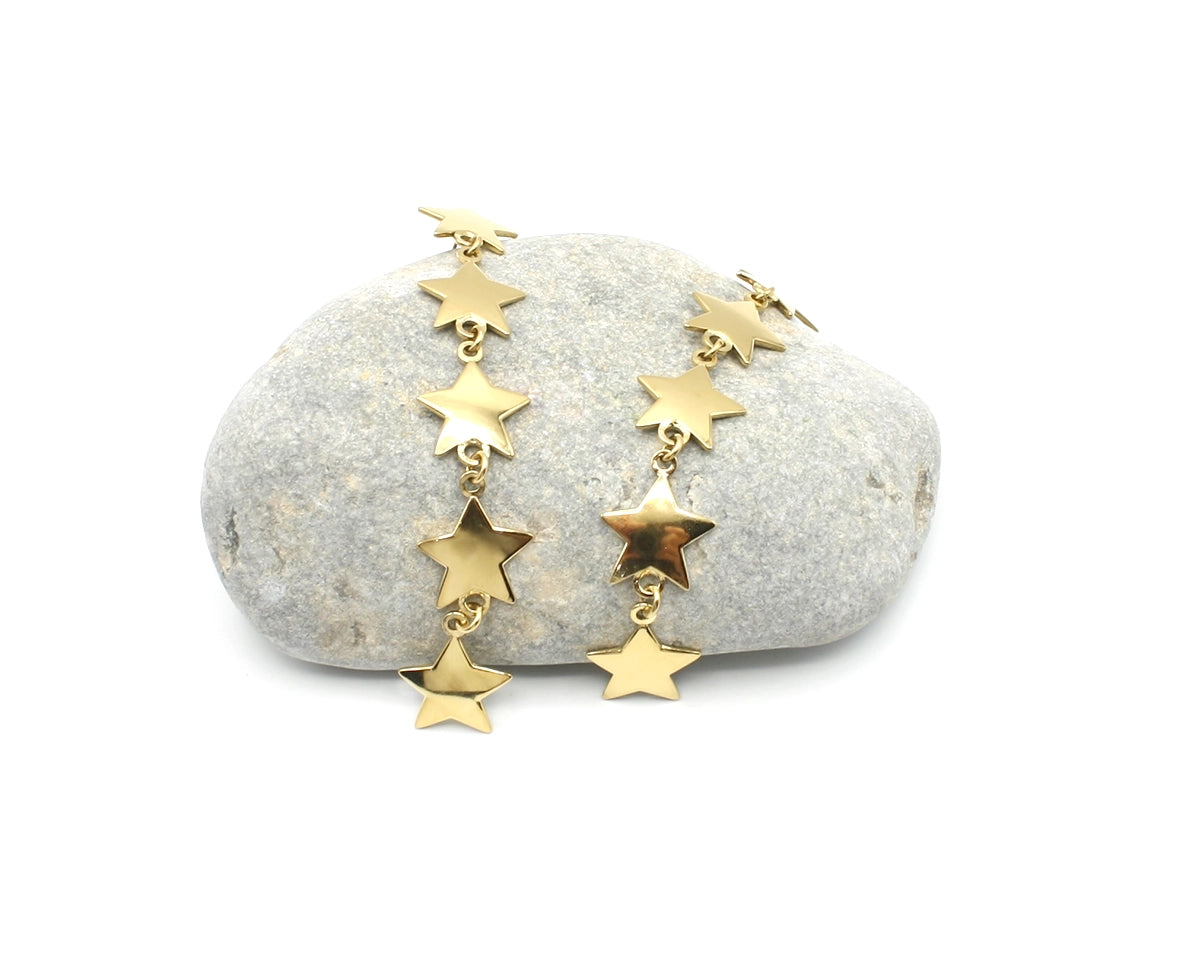 Pendientes largos Georgina acero inoxidable dorado sobre una roca de rio, estrellas doradas brillantes unidas en cascada. DELACABRA 