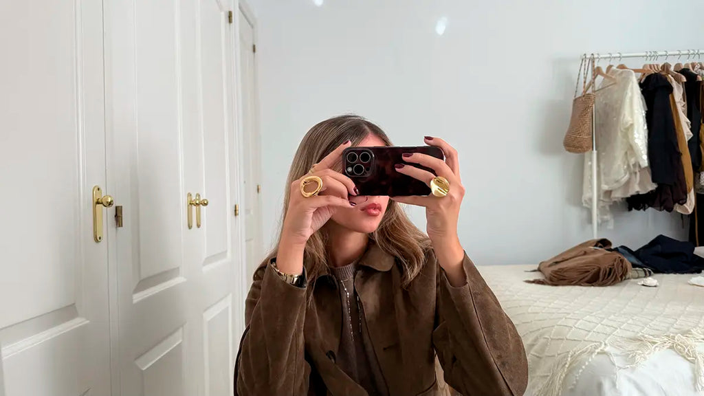 Mujer tomando un selfie, luciendo anillos de Delacabra, en especial el anillo beso, foto en habitación, varios complementos y prendas.