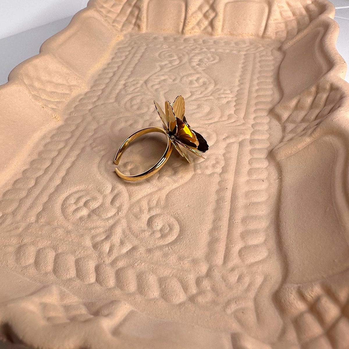 Anillo dorado de acero inoxidable con diseño de colibrí sobre bandeja decorativa beige