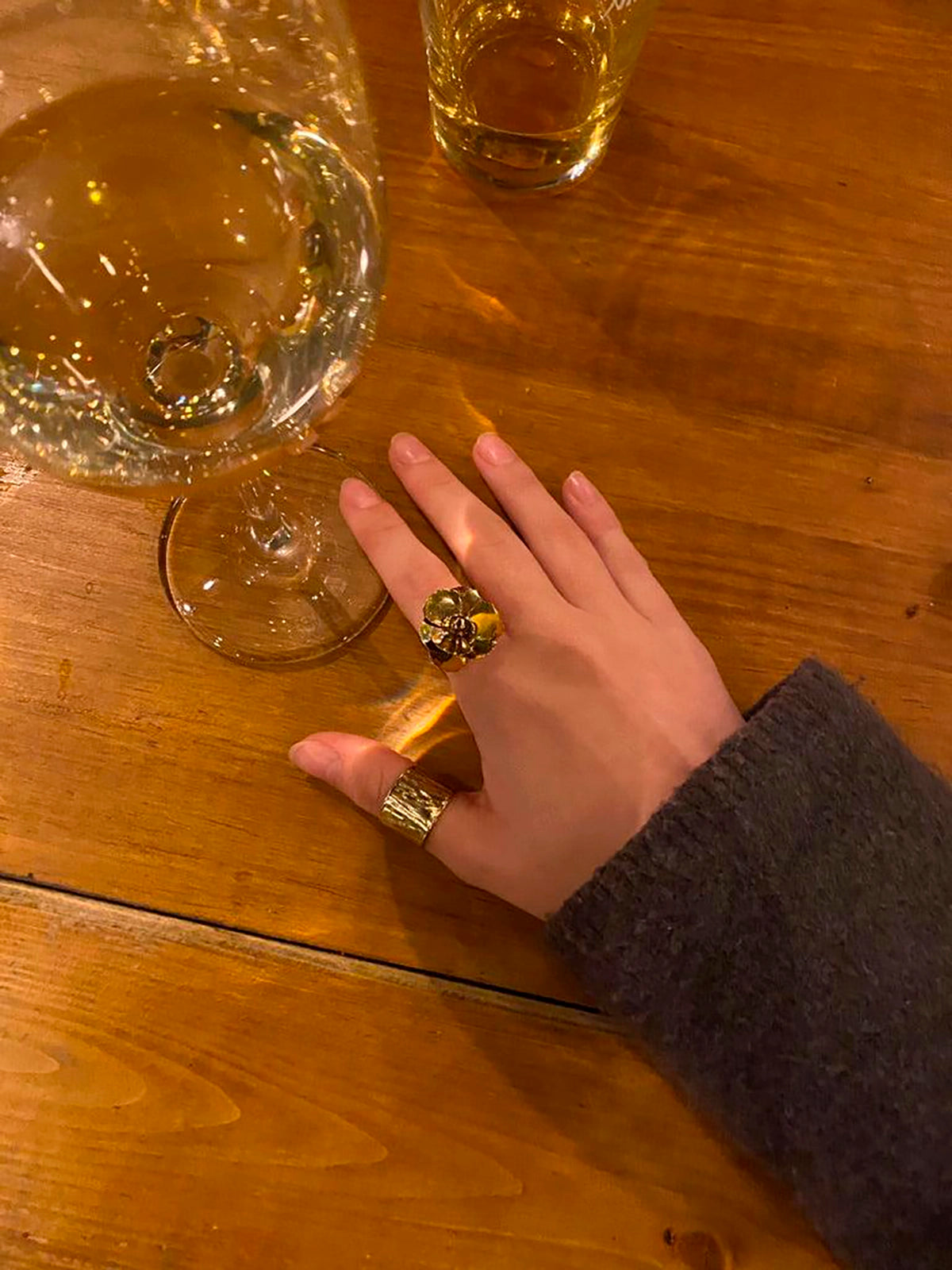 Mano con anillo dorado de colibrí y flor en acero inoxidable sobre mesa de madera