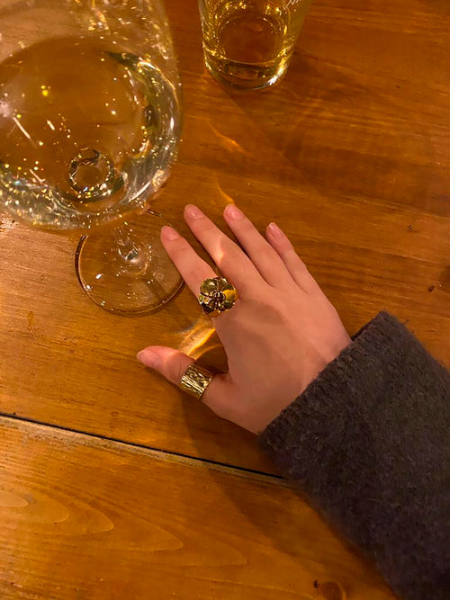 Mano con anillo dorado de colibrí y flor en acero inoxidable sobre mesa de madera