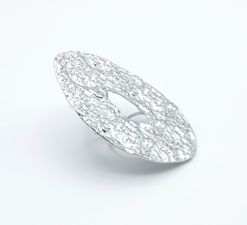 Anillo ajustable GLOOM de DELACABRA en acero inoxidable plateado, con forma ovalada, textura martillada orgánica y abertura central, vista en ángulo