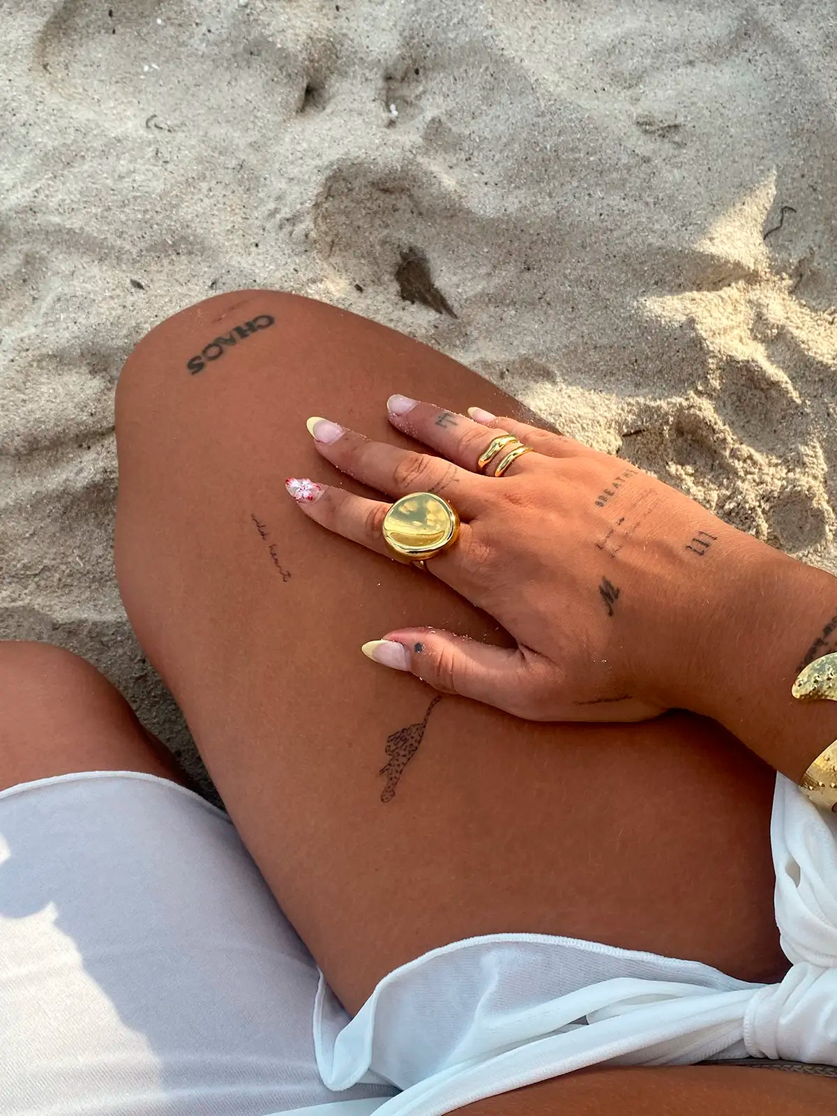 mujer en la playa luciendo anillos entre ellos el double trouble acero inoxidable dorado de delacabra. 