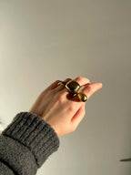 Mano con varios anillos dorados ajustables de acero inoxidable puestos, fotografiada con luz natural y fondo neutro, look invernal con jersey gris