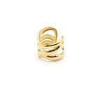 Primer plano del Anillo Nilo de acero dorado en una superficie gris. Se aprecian las tres bandas onduladas y asimétricas, un diseño calado y moderno. Es un anillo abierto y ajustable.