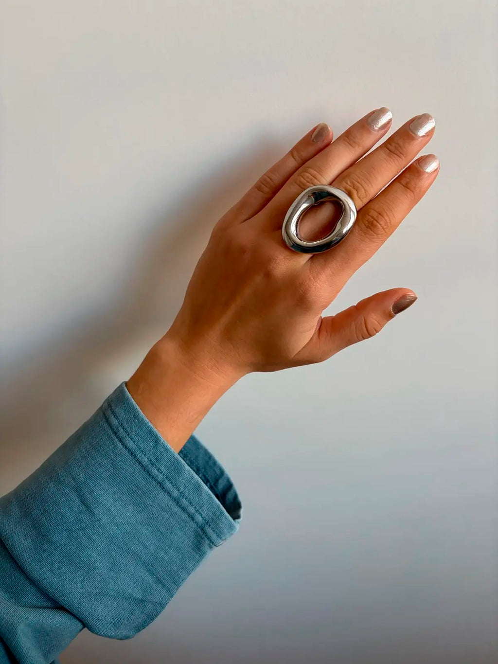 Anillo saturno acero inoxidable dorado ajustable mujer con jersey luce anillo en una toma solo de la mano y parte del brazo. Delacabra