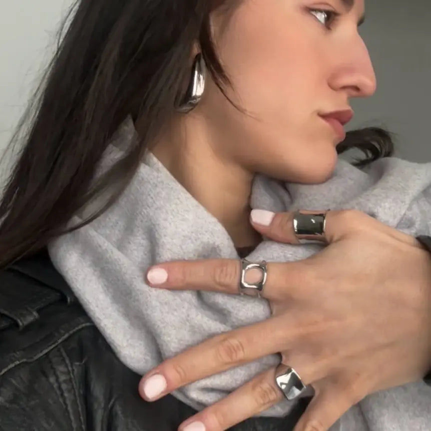 mujer de perfil luciendo anillos y pendientes de Delacabra, con chaqueta de cuero y jersey gris. Delacabra