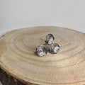 Anillo ajustable de acero inoxidable plateado con diseño de tres flores sobre fondo de madera