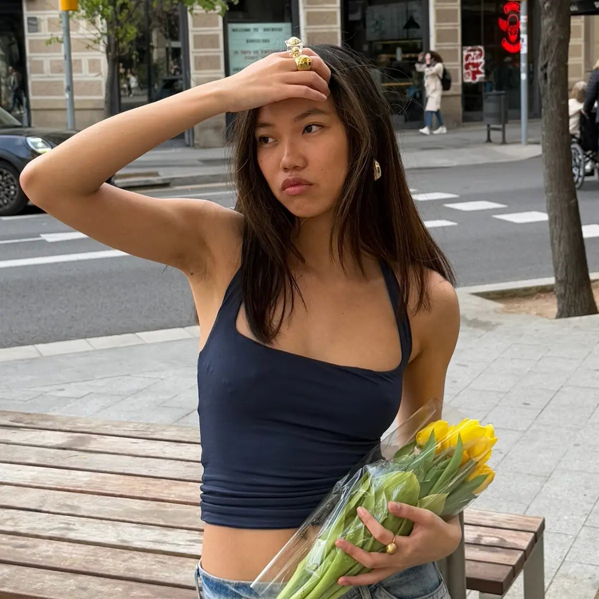 Anillo Venus acero inoxidable dorado, mujer en la callle con flores amarillas en la mano y ropa cómoda y descomplicada, con anillos dorados y pendientes de delacabra