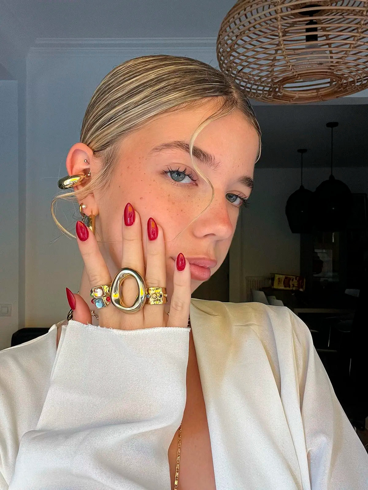 Varios anillos dorados de acero inoxidable de la marca DELACABRA puestos en la mano de una mujer con manicura roja, luciendo un look elegante y sofisticado