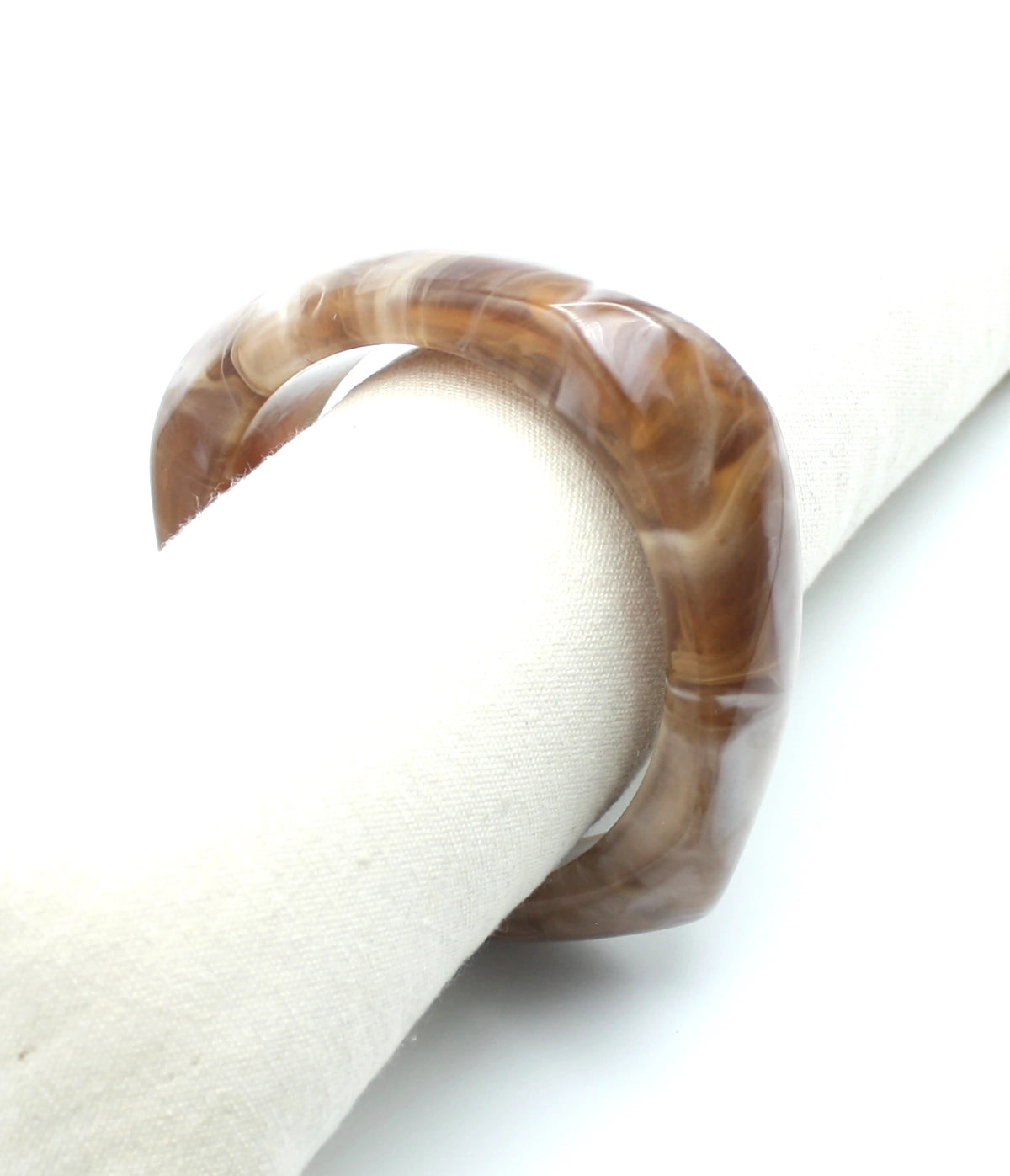 Pulsera Amber de resina marrón translúcida con vetas blancas, sobre soporte cilíndrico de tela beige - DELACABRA