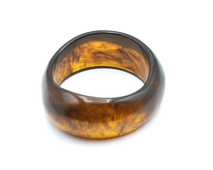 Forma ovalada del brazalete Aura, en resina semitransparente con vetas irregulares en marrón miel - DELACABRA