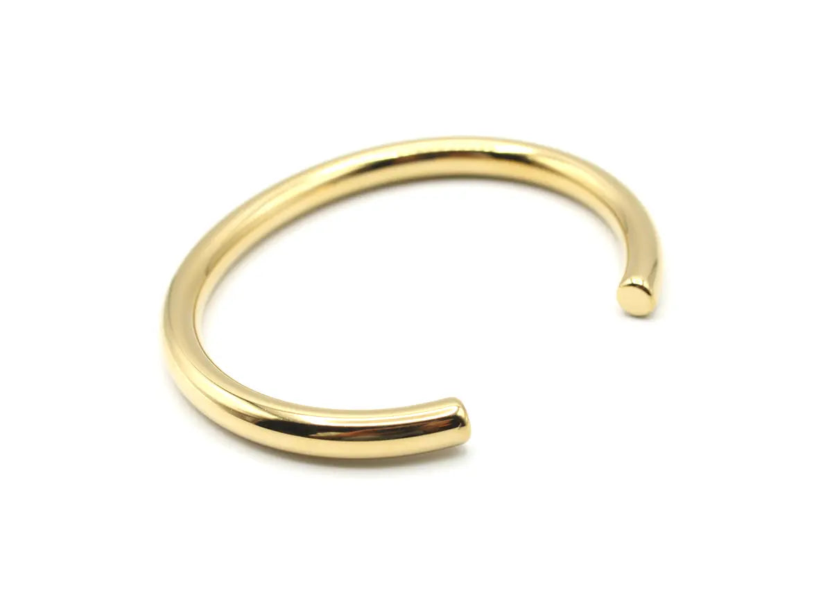 Brazalete rígido Lia dorado con diseño tubular y extremos redondeados. Joya de acero amable con la piel DELACABRA.