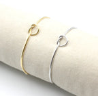 Brazaletes Nude acero inoxidable dorado y plateado con un nudo marinero simple en un expositor de tela, brillante, versátil, resistente al agua. - DELACABRA