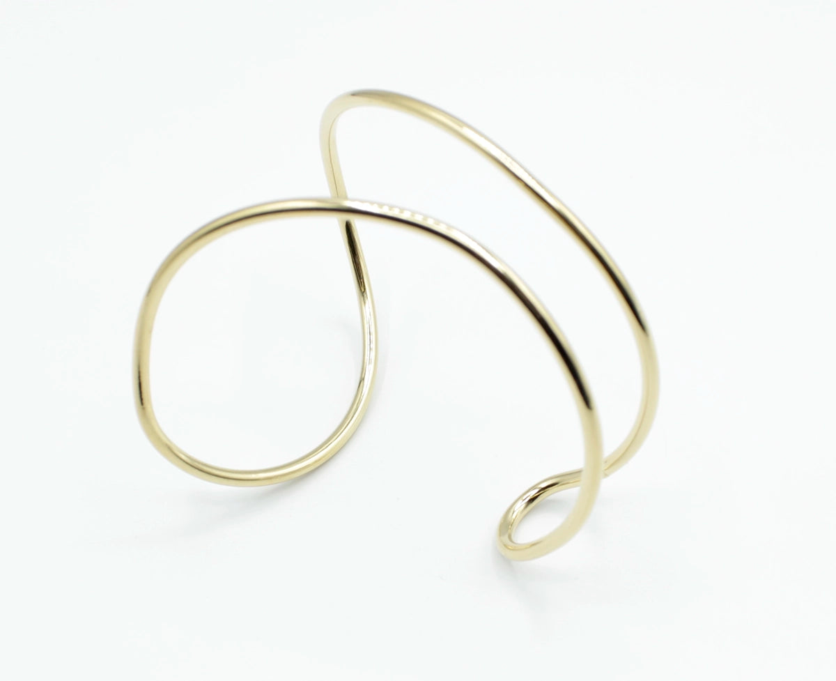 Brazalete Tiana en acero inoxidable dorado, visto desde ángulo elevado con forma fluida y artística, hipoalergénico, resistente al agua, ajustable y duradero -DELACABRA