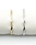 Brazaletes Acqua en acero inoxidable dorado y plateado colocados sobre cojín blanco, diseño retorcido elegante, hipoalergénicos, resistentes al agua, ajustables y duraderos -DELACABRA