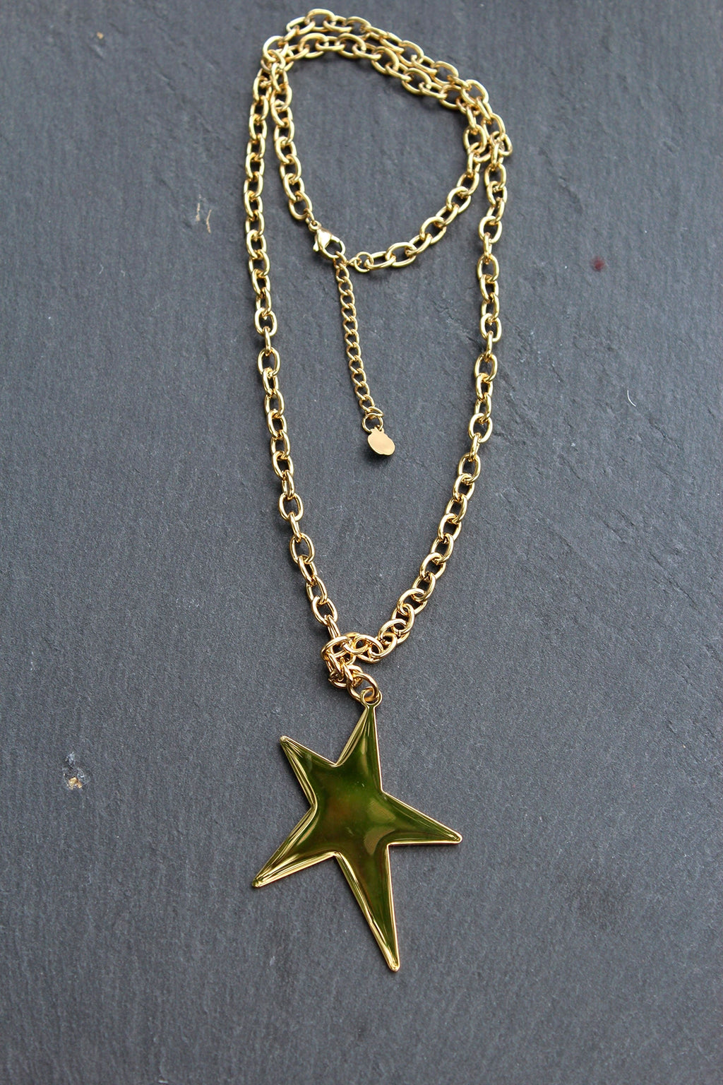 Collar Estrella acero inoxidable dorado sobre una pared gris, cadena de eslabones gruesos, robusto. - DELACABRA