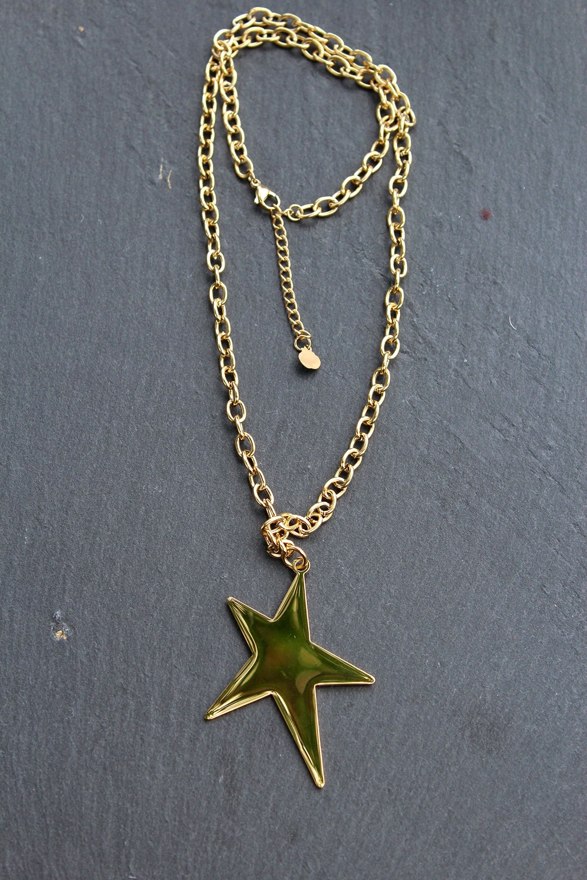 Collar Estrella acero inoxidable dorado sobre una pared gris, cadena de eslabones gruesos, robusto. - DELACABRA