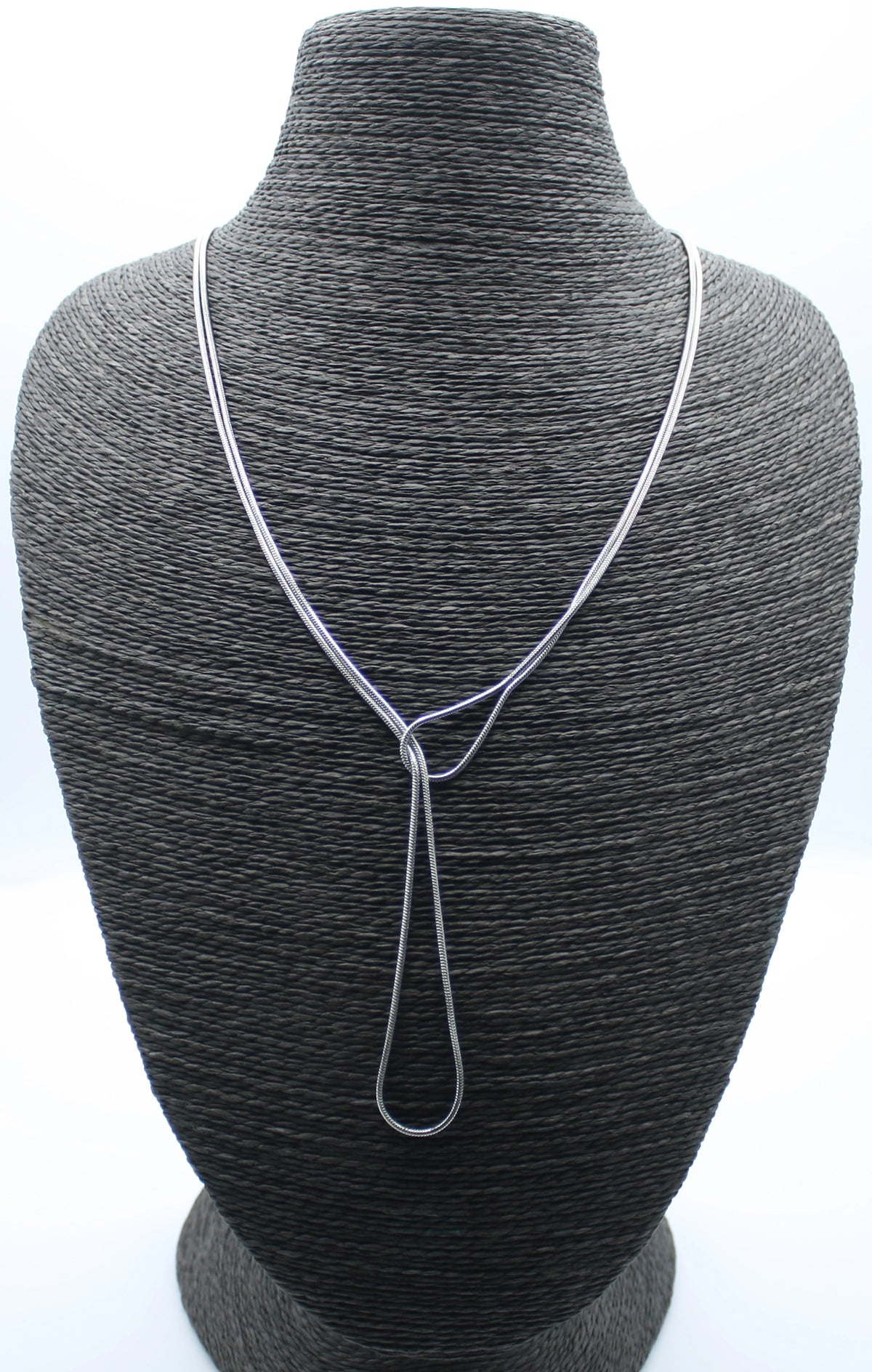 Collar Lazo plateado sobre busto negro. Acero inoxidable hipoalergénico y resistente al agua. Diseño con caída tipo lazo. Pieza atemporal de DELACABRA.