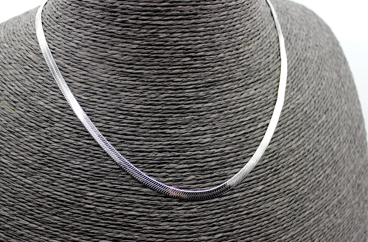 Collar de acero inoxidable plateado estilo cadena serpiente sobre busto negro.