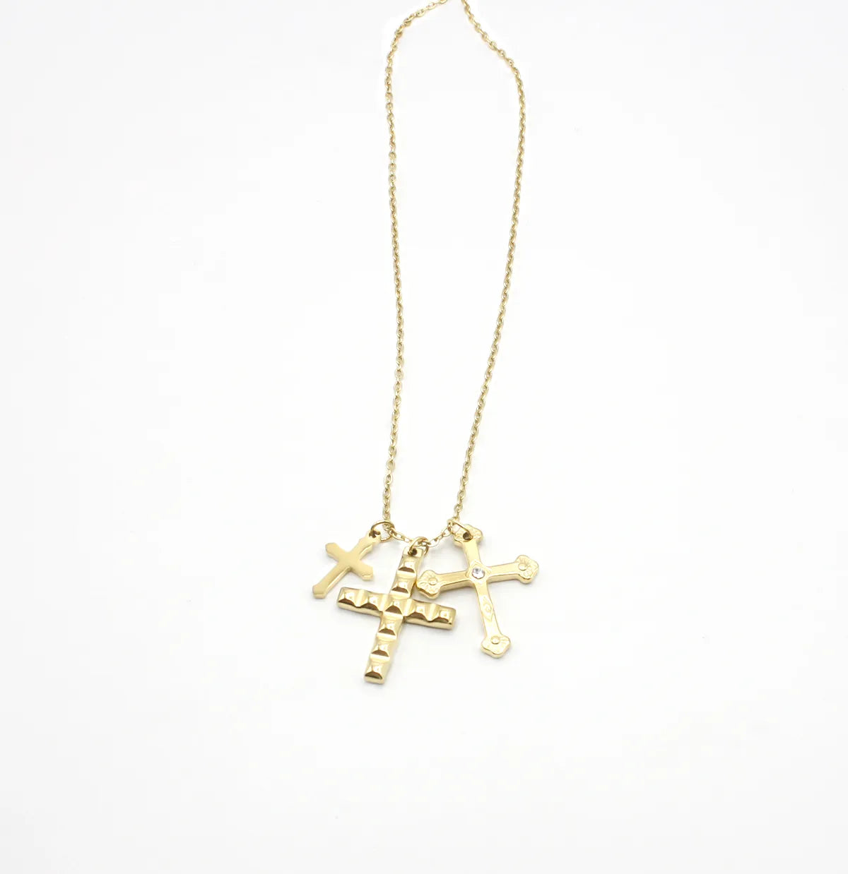 Collar dorado de acero inoxidable con tres dijes de cruces de distintos diseños sobre fondo blanco.