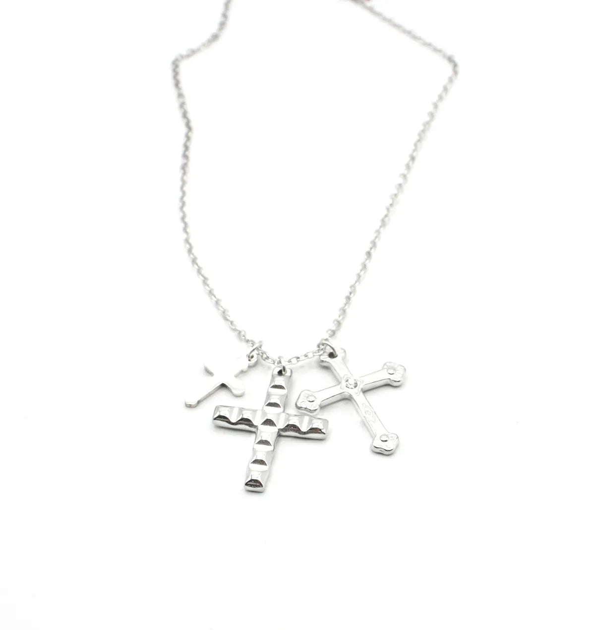 Collar de acero inoxidable plateado con tres dijes de cruces texturizadas, fondo blanco.