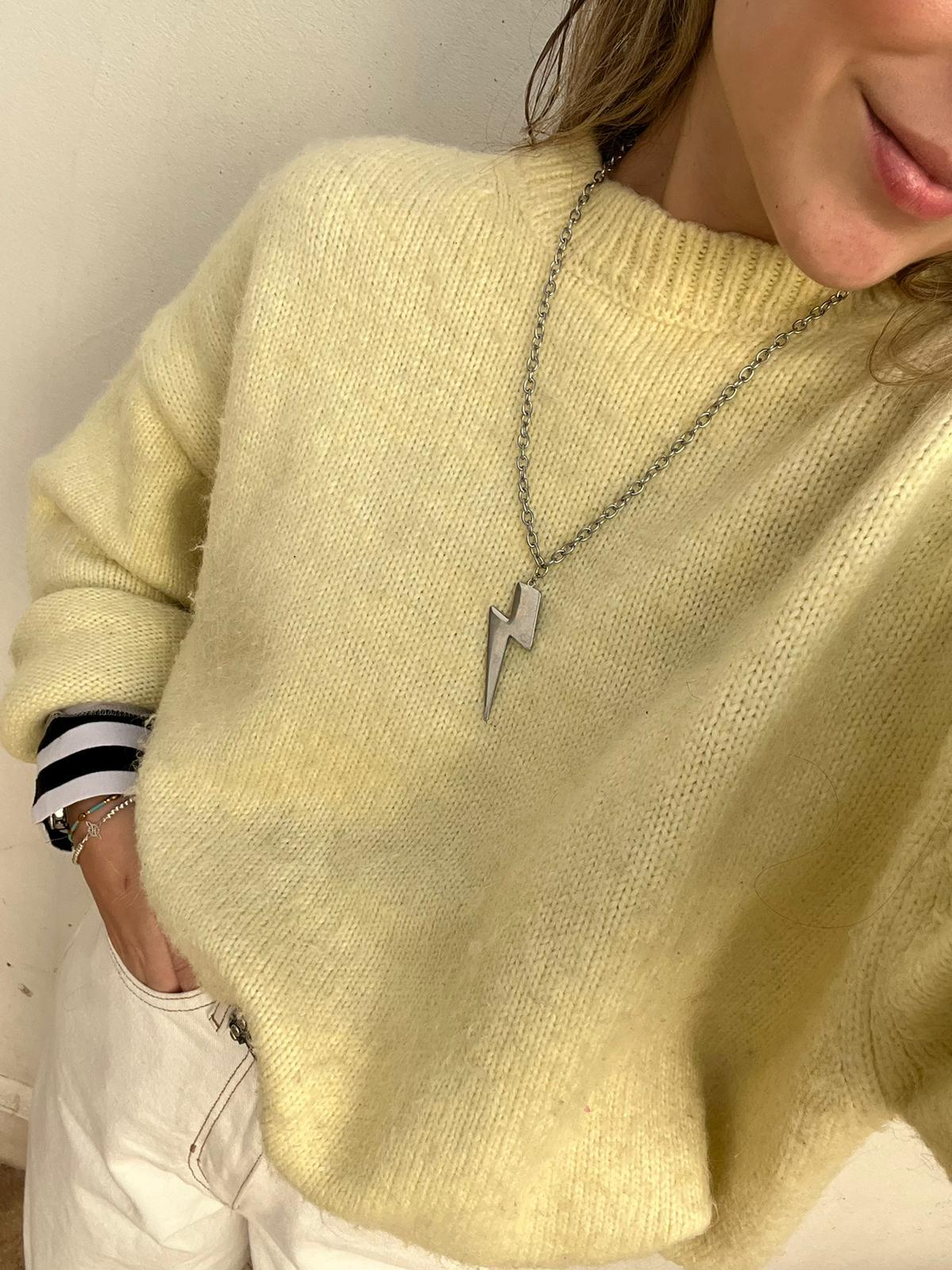 Collar Rayo acero inoxidable plateado, mujer luciendo un jersey amarillo, colgante en forma de rayo grueso, diseño moderno. - delacabra