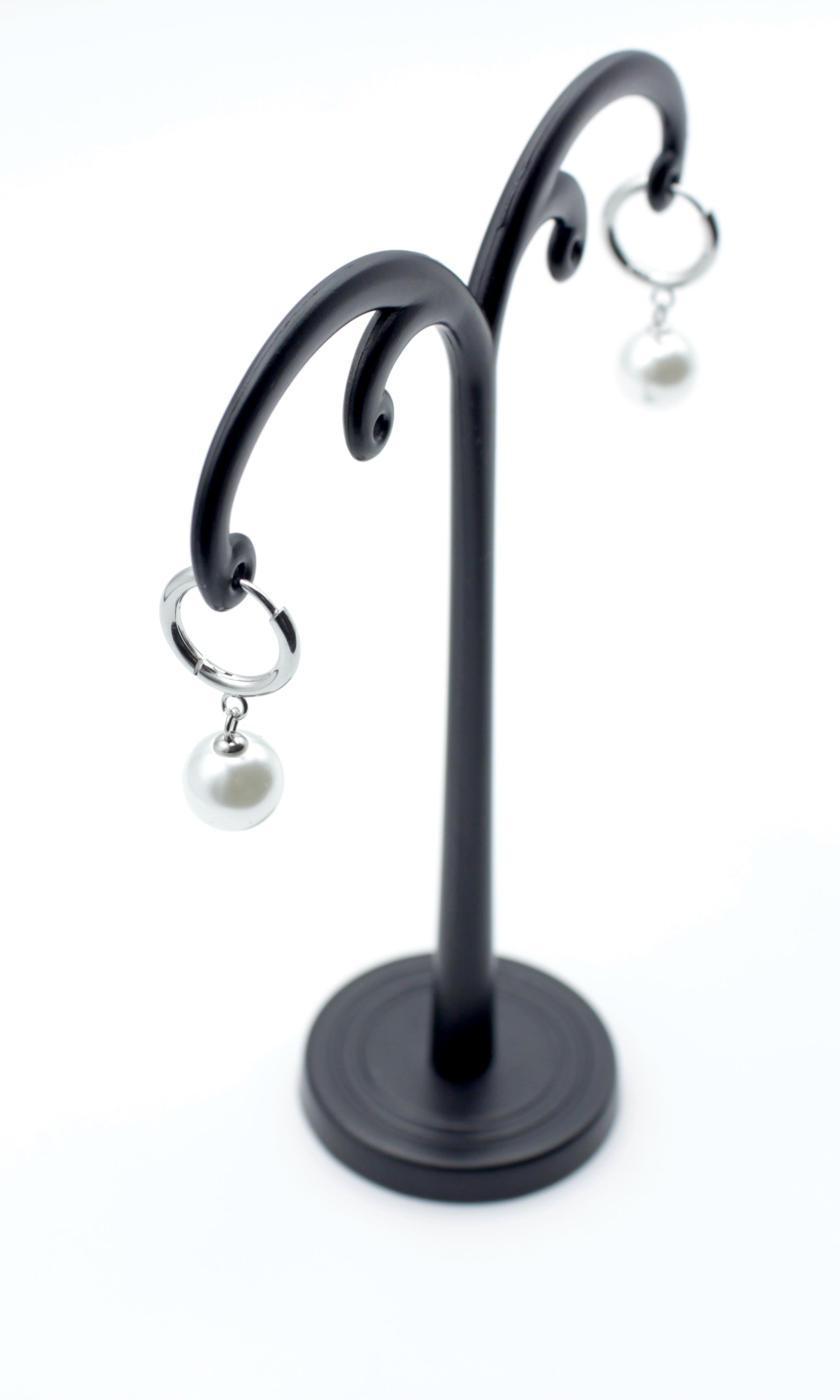 Pendientes Aro Nácar plateados con perla blanca colgante, acero inoxidable hipoalergénico y resistente al agua, vistos en expositor negro.