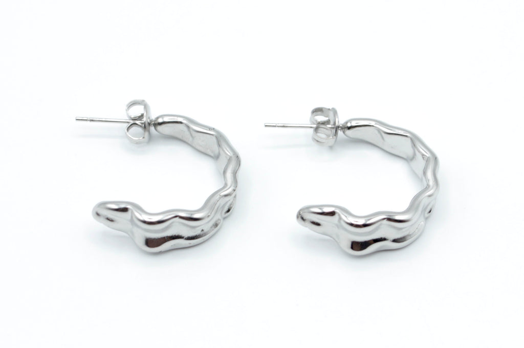 Pendientes Celeste de aro abierto plateado en acero inoxidable hipoalergénico y resistente al agua, con diseño ondulado moderno y cierre mariposa.