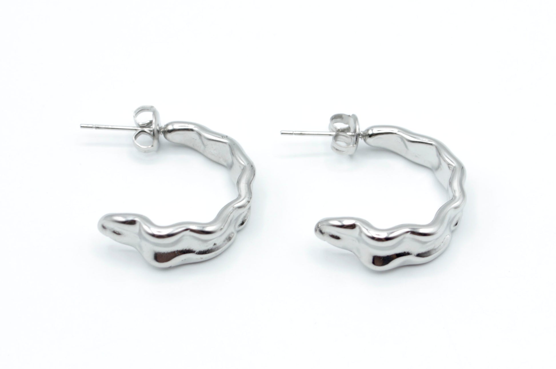 Pendientes Celeste de aro abierto plateado en acero inoxidable hipoalergénico y resistente al agua, con diseño ondulado moderno y cierre mariposa.