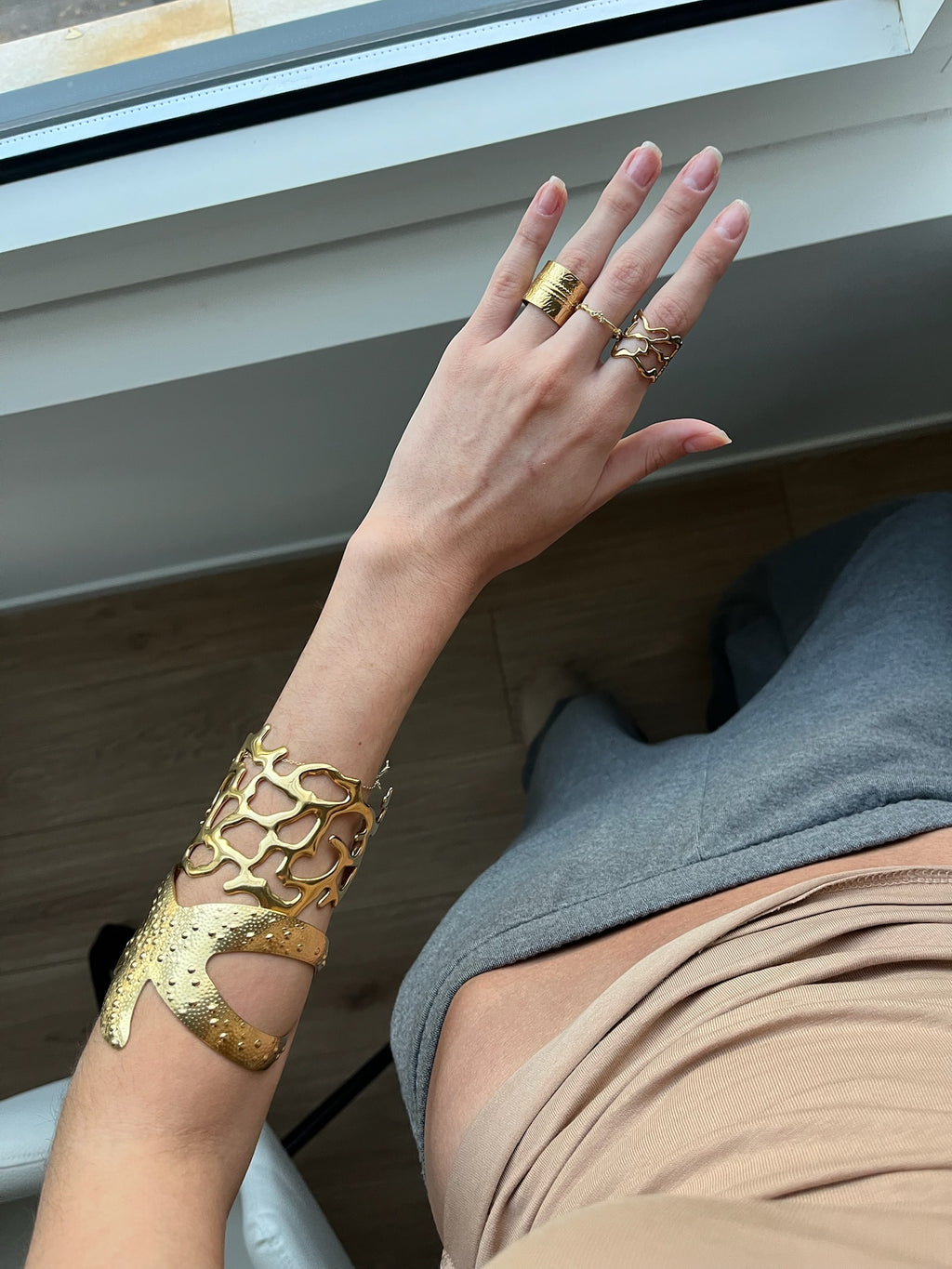 Joyas de acero inoxidable de la marca DELACABRA: anillos y brazalete dorados ajustables, hipoalergénicos y resistentes al agua, lucidos en una mano femenina en plano superior