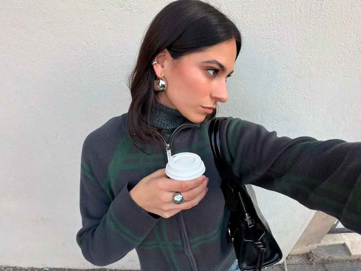 Pendientes aro Angel mujer en look casual tomando café luciendo un jersey oscuro, bolso negro, anillo y pendientes de delacabra